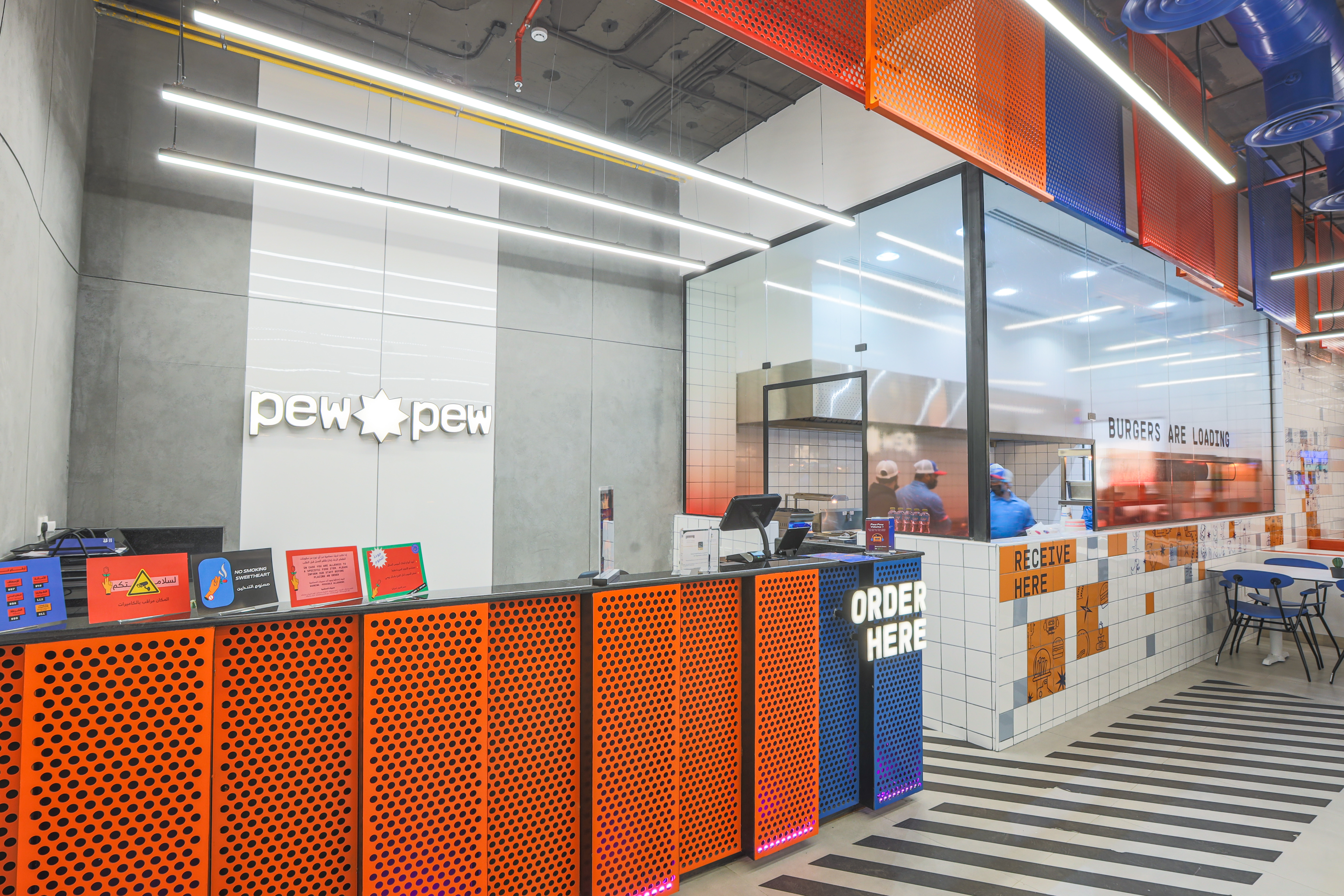 Pew Pew — entrance dining area with blue chairs, glass facade, and neon signage