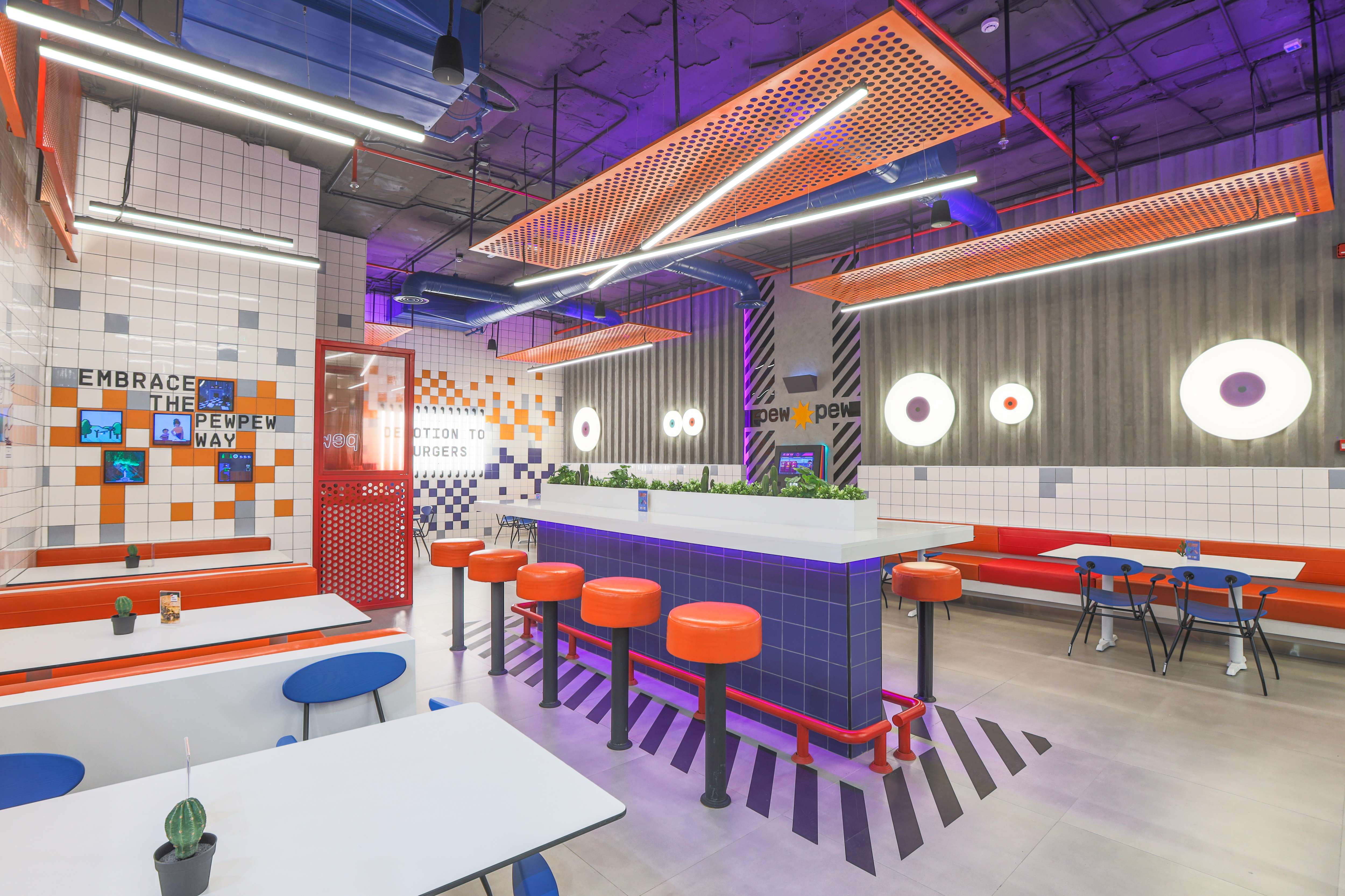 Pew Pew — pop-art tile mural with retro gaming icons under orange perforated ceiling